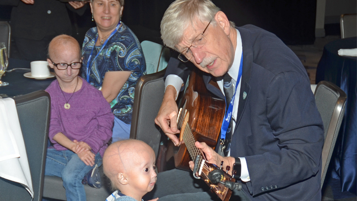 Dr. Collins playing a guitar with children looking on.