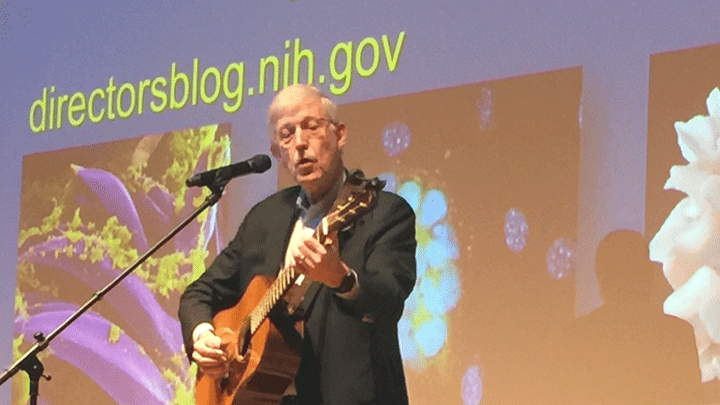 Dr. Francis Collins performs a song on stage at the AJAS Breakfast with Scientists