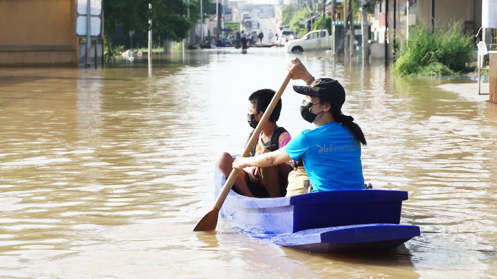 A woman and child in a small boat paddling through flood waters